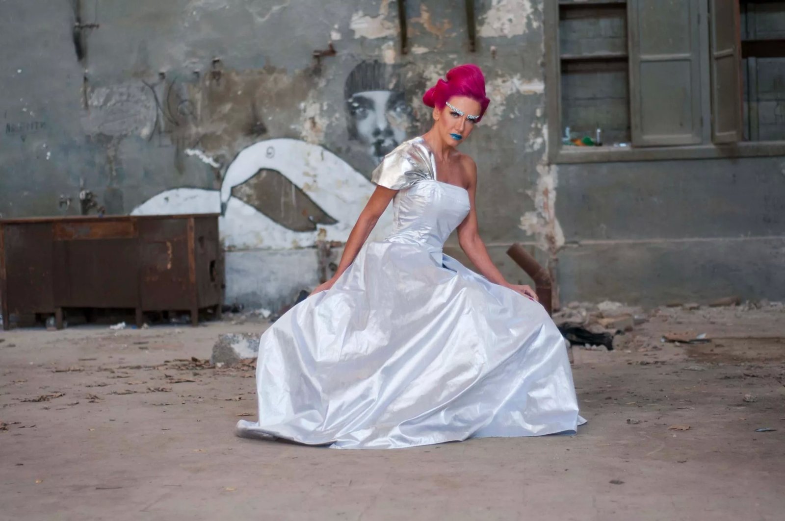 Silver gown seated in an industrial courtyard